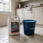 a large UK-brand commercial degreaser bottle placed on a clean tiled kitchen floor beside a sturdy plastic bucket filled with clear water and a faint soap tint